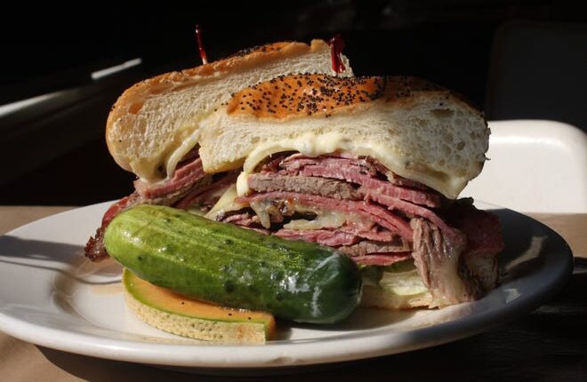 The Gutty at Mudgie's Deli in Detroit's Corktown neighborhood combines layers of warm, top-quality meats -- house-roasted corned beef and beef brisket, Genoa salami, pastrami and bacon -- with Romaine and garlic mayo on a Kaiser roll.  A big pickle brings some crunch to the plate.  Picture taken at Mudgie's Deli on August 4, 2012.