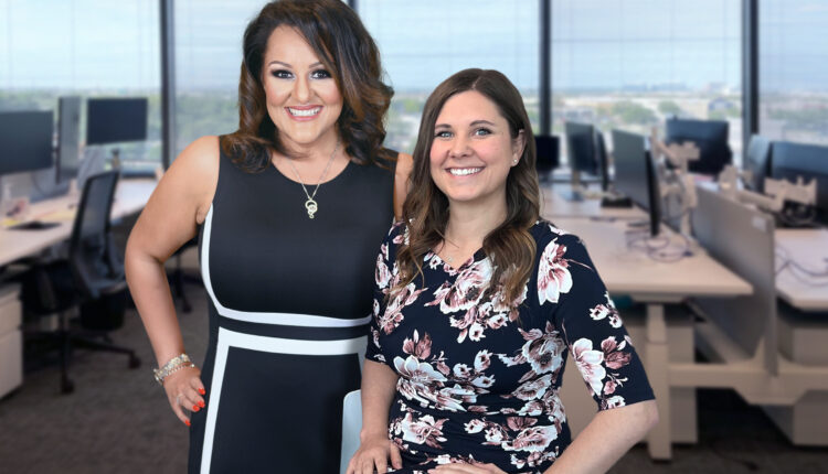 Ruby Gadelrab (left) stands next to Katie Coleman (right). They both are smiling widely at the camera. The background shows their office, out of focus.