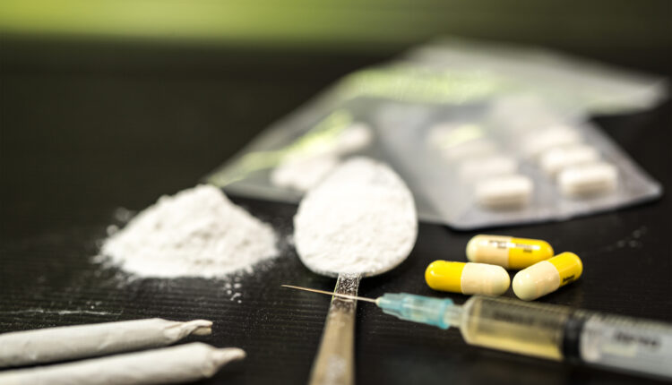A photo shows a syringe and an array of illegal drugs.