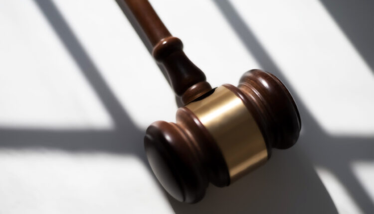 A photo shows a judge's gavel resting on a surface surrounded by shadows.