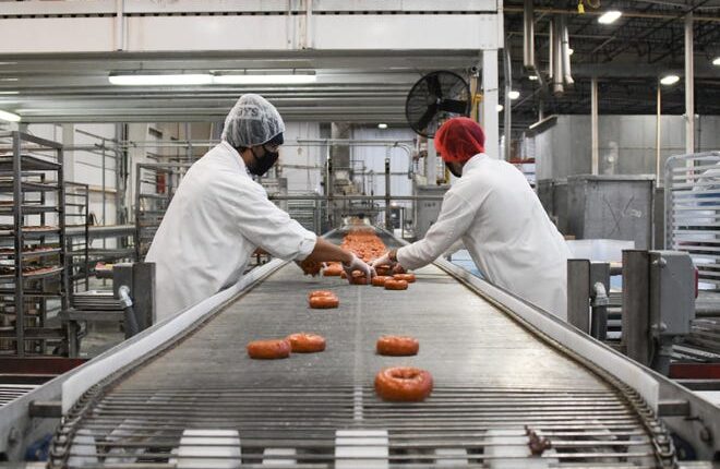 Jaime Salinas, left, and Matt Cooley cull freshly-baked donuts from the line at the Quality Dairy Bakery Plant in REO Town, Monday, Feb. 1, 2021 in Lansing.