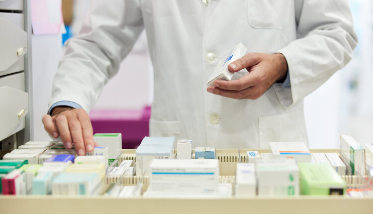 A photo of a pharmacist organizing boxes of pills in an opened drawer.
