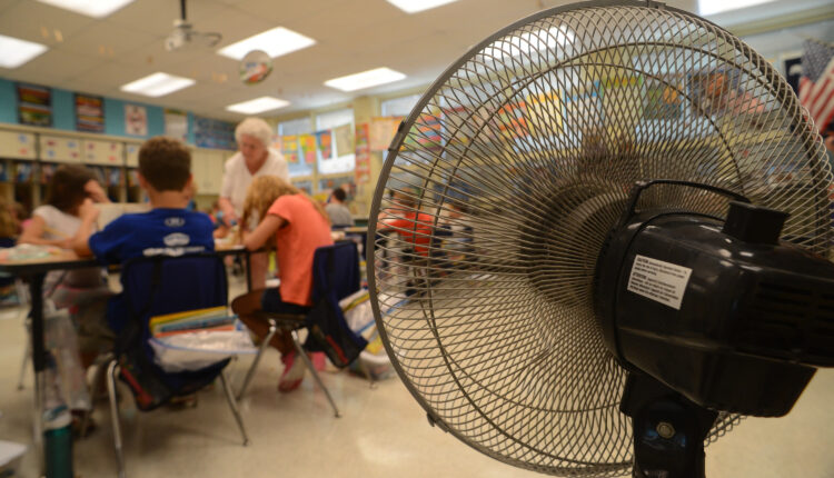 A photo of a fan setup in a classroom as a teacher helps students with their work.